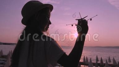 剪影女孩在日落时在热带海滩玩玩具飞机。 手拿<strong>小飞机</strong>特写.. 放松时间